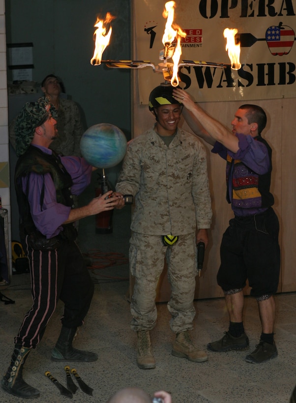 CAMP BLUE DIAMOND, AR RAMADI, Iraq - Corporal Vladimir J. Espinal, a 22-year-old member of the camp's quick reaction force and New York native, is geared up to assist the juggling comic team, Dan Thurmon (right) and Todd Key  (left) during Operation Swashbuckle. The team is part of a four-man comedy show presented by Hack and Slash, who provided an explosive round of entertainment for more than 100 Marines, sailors and soldiers here serving with the 2nd Marine Division in support of Operation Iraqi Freedom.