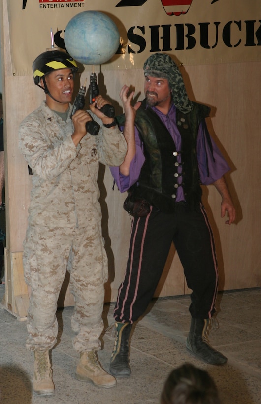 CAMP BLUE DIAMOND, AR RAMADI, Iraq - Corporal Vladimir J. Espinal, a 22-year-old member of the camp's quick reaction force and New York native, is taught how to switch a spinning ball from one hand drill to the nest by juggler, comedian and trickster, Todd Key, during Operation Swashbuckle. Keys is part of a four-man comedy show presented by Hack and Slash, who provided an explosive round of entertainment for more than 100 Marines, sailors and soldiers here serving with the 2nd Marine Division in support of Operation Iraqi Freedom.