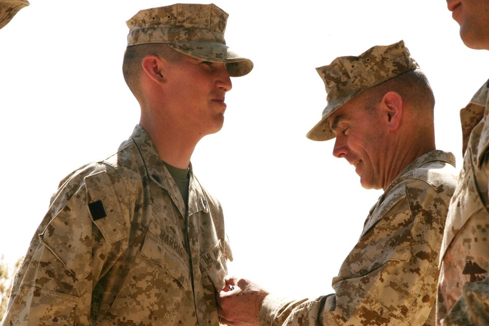 CAMP BLUE DIAMOND, Iraq - Brigadier Gen. Joseph J. McMenamin, assistant division commander for 2nd Marine Division, awards Cpl. Justin Harris, a 23-year-old light armored vehicle technician with 2nd Light Armored Reconnaissance, with a Purple Heart, April 8, for injuries he received from a roadside explosion.  An improvised explosive device (IED), used by insurgents as a way to inflict collateral damage from a distance, rocked through two convoys as they passed one another in opposite directions on a dirt road near the base, March 13.  Harris and his team were providing security on the road from within their Light Armored vehicles and Humvees.  U.S. Marine Corps photo by Sgt. Stephen D'Alessio (RELEASED)