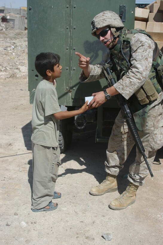 AR RAMADI, Iraq (May 26, 2005) - Corporal Michael L. Godfrey, assistant noncommissioned officer with Team 1, Detachment 3, 5th Civil Affairs Group, which is in direct support of 1st Battalion, 5th Marine Regiment, gives an Iraqi boy a watch and tells him to get his friends so they can get a gift during a mission here. The 21-year-old from Mount Zion, Md., and fellow 5th CAG Marines and Marines with 4th Platoon, Company C conducted a civil affairs mission at the Al Jaod Elementary School here. The Marines surveyed the school and determined what repairs and supplies are needed. Photo by: Cpl. Tom Sloan