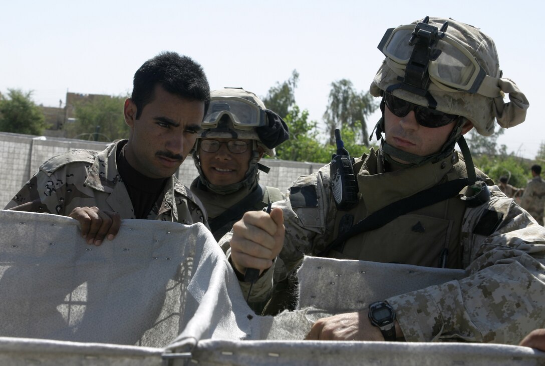 FALLUJAH, Iraq - Cpl. Allen Ryals, 2nd Squad leader, 2nd Platoon, Company A, 2nd Combat Engineer Battalion, right, cuts through the canvas of a Hesco barrier in an Iraqi soldiers' base of operations here May 26 as fellow engineer, Lance Cpl. Mario Castillo, and an Iraqi soldier, observe.  Ryals' engineers worked alongside the Iraqi soldiers to teach them how to properly fortify one of their headquarters in the city by laying out barricades and stretching out wire.