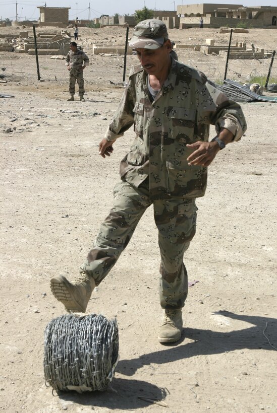 FALLUJAH, Iraq - An Iraqi soldier kicks a spool of concertina wire in his base of operations here May 26, as he moves it to the location where he and fellow soldiers will stretch it out to protect their position.  Marines from 2nd Combat Engineer Battalion worked alongside the soldiers to teach them how to properly fortify one of their headquarters in the city by laying out barricades and stretching out wire.