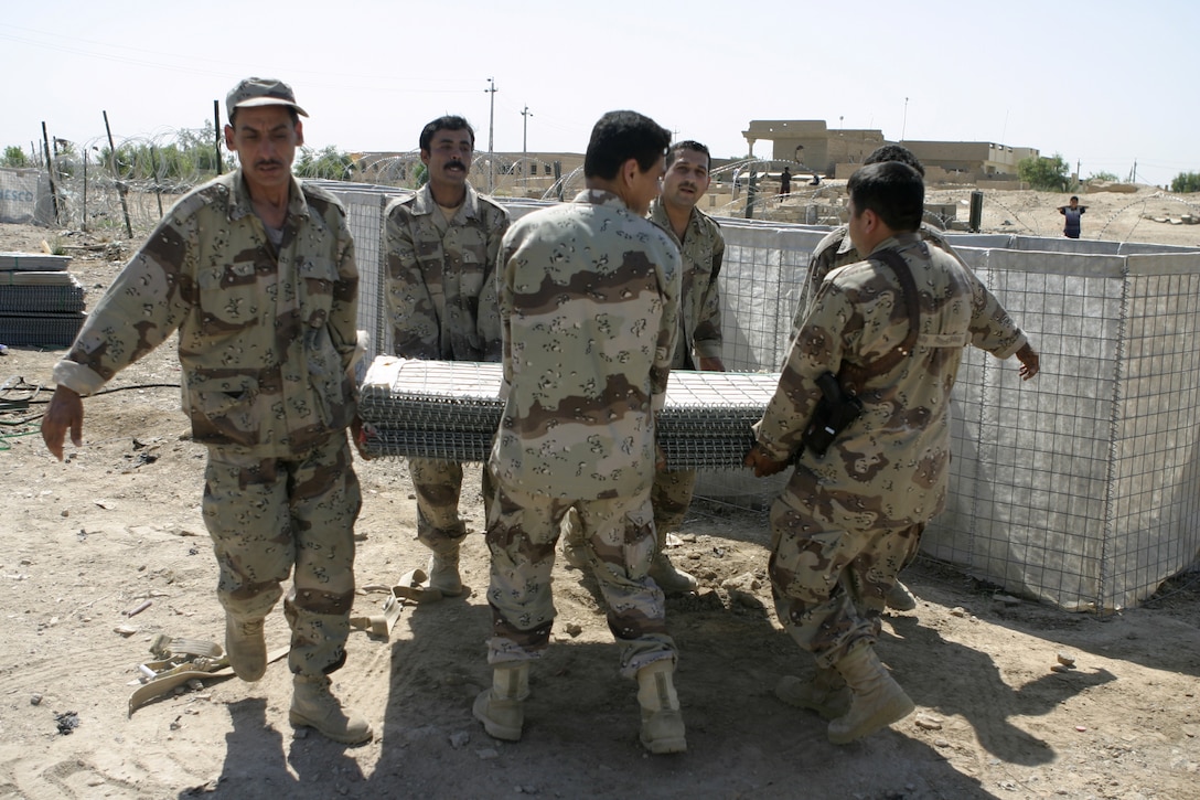 FALLUJAH, Iraq - Iraqi soldiers carry away a stack of Hesco barriers as they prepare to stretch them out to fortify their base of operations here May 26.  Marines from 2nd Combat Engineer Battalion worked alongside the soldiers to teach them how to properly fortify one of their headquarters in the city by laying out barricades and stretching out wire.