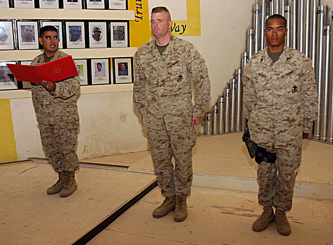 CAMP BAHARIA, Iraq - CAMP BAHARIA, Iraq - Staff Sgt. Candelario Martinez Jr., 1st Battalion, 6th Marine Regiment's career retention specialist, back left, reads a certificate of re-enlistment for Cpl. Anthony Booker, front right.  Martinez, a 35-year-old Eagle Pass, Texas native, assists his fellow Marines plan their future careers, whether inside the military or out in the civilian world.