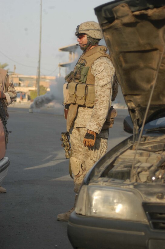 AR RAMADI Iraq (July 25, 2005) - Sergeant Fidel A. Alcoces, the platoon sergeant for 2nd Platoon, Company A, 1st Battalion, 5th Marine Regiment, stands in front of a vehicle with its hood up during a mission in the city here July 25. A smoke bomb in the distance shoots thick, gray smoke into the air give 29-year-old Alcoces from San Antonio, Texas and his fellow Marines cover from enemy snipers while they operated in the open. Marines with the Camp Pendleton, Calif., -based infantry battalion conducted a battalion-wide operation in the city's marketplace, where they searched vehicles and personnel for weapons and improvised explosive making material. Photo by: Cpl. Tom Sloan