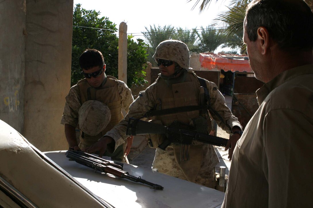 BARWANA, Iraq (Oct. 26, 2005)  - An Iraqi citizen looks on as Cpl. Ralph E. Arzate of Victorville, Calif. and an interpreter gather information about each house in the community here Oct. 26. Arzate, a squad leader, and other Marines with L Company, 3rd Battalion, 1st Marine Regiment, gathered information like names, number of people in family, weapons in the house, occupations and vehicles they drive for use on future operations. (Official Marine Corps photo by Cpl. Adam C. Schnell)