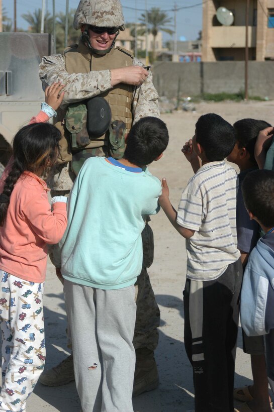 AR RAMADI, Iraq (March 27, 2005) - Navy Lt. Aaron T. Miller, chaplain for 1st Battalion, 5th Marine Regiment, reaches in his blouse pocket for candy to give to Iraqi children outside observation post Ghetto here. The 32-year-old man of God from Redlands, Calif., visited Marines from the infantry battalion's five companies of whom he preached a hasty Easter service and served Holy Communion to. The effort, which lasted more than six hours, required Miller to travel to seven different places in the city where Marines are serving. Photo by Cpl. Tom Sloan