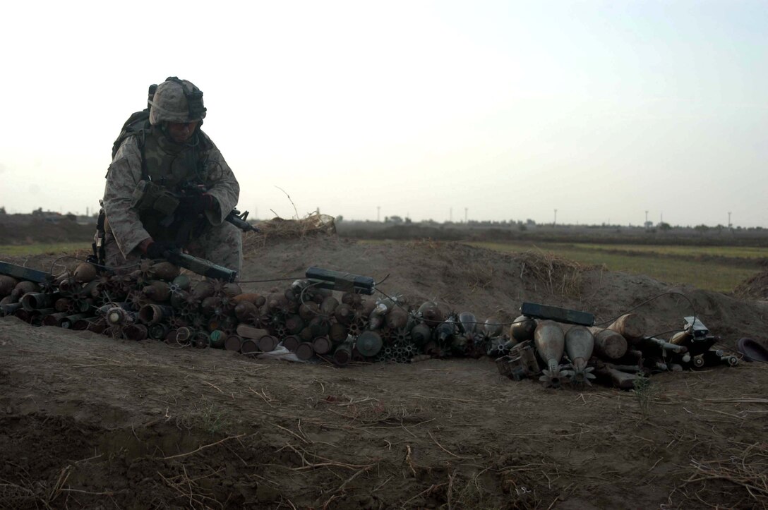 AR RAMADI, Iraq (April 26, 2005) - Staff Sgt. Ray A. Valdez, guide, 4th Platoon, Company A, 1st Combat Engineer Battalion, kneels down and secures C-4 plosives on a pile of illegal weapons he and his Marines discovered buried on farmland on the southern outskirts of the city here. The 30-year-old from San Antonio, Texas and his fellow engineers found 15 AK-47s; 12 bolt action rifles; three RPK machine guns; three rocket propelled grenade launchers; 200 60 mm shells, 100 82 mm shells; 20 120 mm shells; 10 155 mm shells; 40 pounds of P-C4 explosives; 30 hand grenades and 50 52 mm high explosive anti-tank missiles during their mission that had them trudging through the fields for more than 16 hours. The blast masters destroyed the weapons caches with controlled detonations so insurgents can no longer use them against coalition forces. Photo by Cpl. Tom Sloan