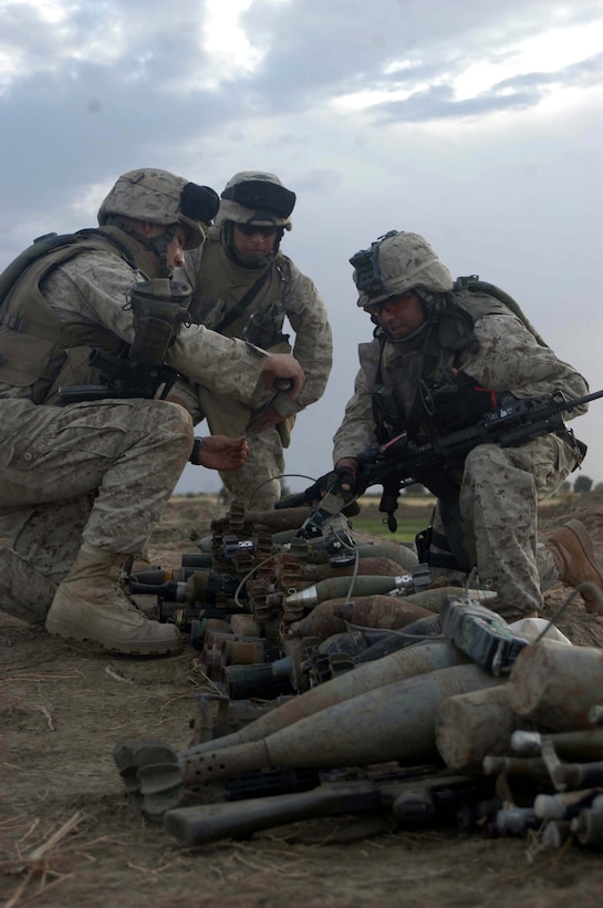 AR RAMADI, Iraq (April 26, 2005) - Private First Class Brandon H. Griffin,(left) Sgt. Miguel A. Cira(center) and Staff Sgt. Ray A. Valdez, combat engineers with 4th Platoon, Company A, 1st Combat Engineer Battalion, apply C-4 plosives on a pile illegal weapons they and other Marines with their platoon discovered buried on farmland on the southern outskirts of the city here. The engineers found 15 AK-47s; 12 bolt action rifles; three RPK machine guns; three rocket propelled grenade launchers; 200 60 mm shells, 100 82 mm shells; 20 120 mm shells; 10 155 mm shells; 40 pounds of P-C4 explosives; 30 hand grenades and 50 52 mm high explosive anti-tank missiles during their mission that had them trudging through the fields for more than 16 hours. The blast masters destroyed the weapons caches with controlled detonations so insurgents can no longer use them against coalition forces. Photo by Cpl. Tom Sloan