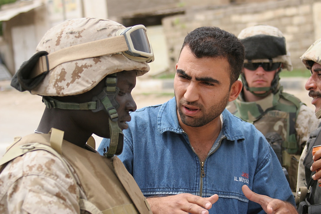Haqlaniyah, Al Anbar, Iraq.-- An Iraqi civilian speaks through a translator to the Marines of 5th Civil Affairs Group, Detachment 4, Team 4.  Interpreters integrate into the CAG team to better assist and understand the needs of the community.  Marines are sometimes handed written claims from civilians who approach them while on patrol.  The CAG team evaluates these claims and determines whether compensation is due.     (Photo by LCpl. Marc Fencil. )