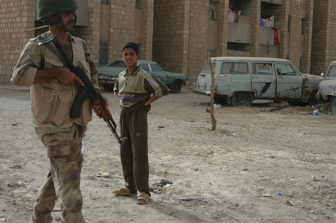 AR RAMADI Iraq (June 27, 2005) - A young, Iraqi boy watches a member of the Iraqi Security Forces patrol through his neighborhood in the city here June 26. Marines with the Combined Action Platoon, Company B, 1st Battalion, 5th Marine Regiment, train new members of the ISF at their base, Camp Ali. After 12 days of intense training, the ISF conduct missions alongside other elements of the infantry battalion to further hone their military skills. Photo by: Cpl. Tom Sloan