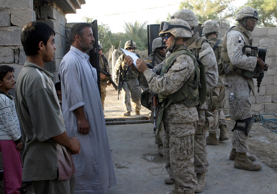 SAQLAWIYAH, Iraq - Remy, an interpreter, speaks with Iraqi citizens outside a home here July 27 during Operation Hard Knock, while Marines with Company A, 1st Battalion, 6th Marine Regiment provide security nearby.  Company A Marines searched dozens of houses throughout the small township outside Fallujah, looking for weapons, explosives and insurgent activity while gathering census data on the populace there.  The Marines apprehended one suspected insurgent supporter.