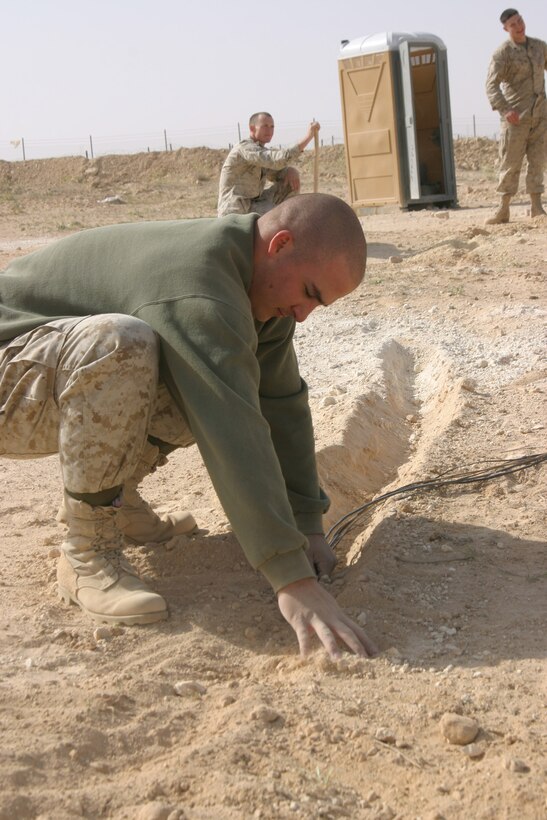 Corporal Ron Damangue, satellite operator, Marine Wing Communications Squadron 28 and Houma, La., native, places communications wire into a freshly dug ditch aboard Forward Operating Base Al Qaim.