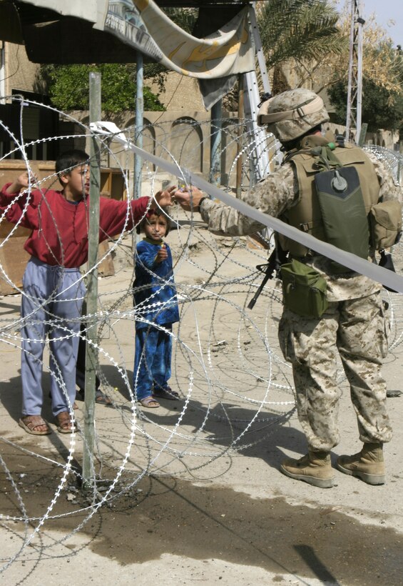 FALLUJAH, Iraq - A Marine with 1st Battalion, 6th Marine Regiment reaches through a wire barrier in the Jolan Park compound here to hand two Iraqi children some candy.  1st Battalion, 6th Marine Regiment personnel are assisting the Iraqi Interim Force and Public Order Battalion police force to provide security in the distribution of $100 million worth of reparation payments to citizens to rebuild their homes and businesses from damages done during the assault on Fallujah last year.