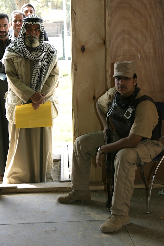 FALLUJAH, Iraq - A guard with the Public Order Battalion Iraqi police force watches over a line of people waiting to receive reparation payments at the Jolan Park compound here.  POB personnel and the Interim Iraqi Forces are working alongside Regimental Combat Team-8 to provide security in the distribution of $100 million worth of reparation payments to citizens to rebuild their homes and businesses from damages done during the assault on Fallujah last year.