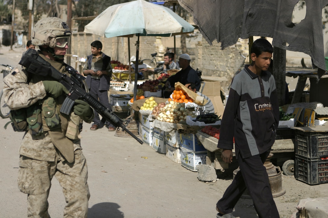 FALLUJAH, Iraq - A Marine with 4th Platoon, Company B, 1st Battalion, 6th Marine Regiment, provides security for his patrol as they pass through an Iraqi market place near the Jolan Park compound area here.  Company B Marines are working alongside Interim Iraqi Forces to provide security to the reparation payment issue sight.