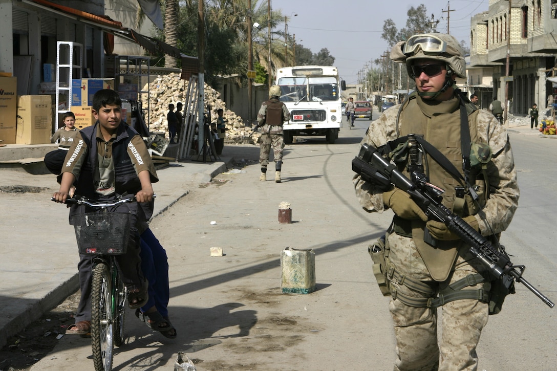FALLUJAH, Iraq - Lance Cpl. Matthew R. Levy, a machine gunner with 4th Platoon, Company B, 1st Battalion, 6th Marine Regiment, walks alongside an Iraqi boy on a bicycle while patrolling the streets near the Jolan Park compound area here.  Company B Marines are working alongside Interim Iraqi Forces to provide security to the reparation payment issue sight.
