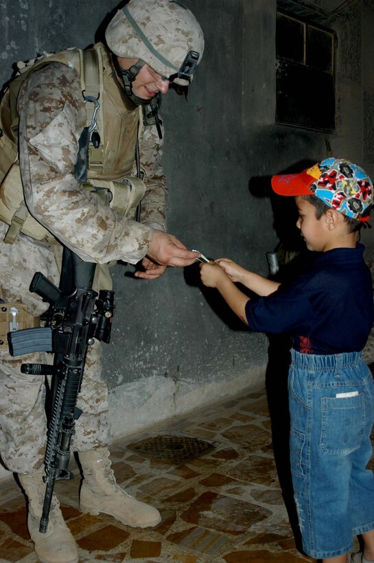 AR RAMADI Iraq (July 19, 2005) - Sergeant Aaron P. Selby, 3rd Squad leader, 1st Platoon, Company C, 1st Battalion, 5th Marine Regiment, gives a young, Iraqi child a piece of chewing gum during a mission in the city here July 19. The 26-year-old from Ft. Thomas, Ky., is a husband a father of two. Nicole, his wife of six years, their three-year-old daughter Amara and two-year-old son Memphis are at home in Oceanside, Calif., while he fights the war on terror halfway around the world. The Selbys will be reunited in October after seven months of separation when 1st Battalion, 5th Marines return to Camp Pendleton, Calif. Photo by: Cpl. Tom Sloan