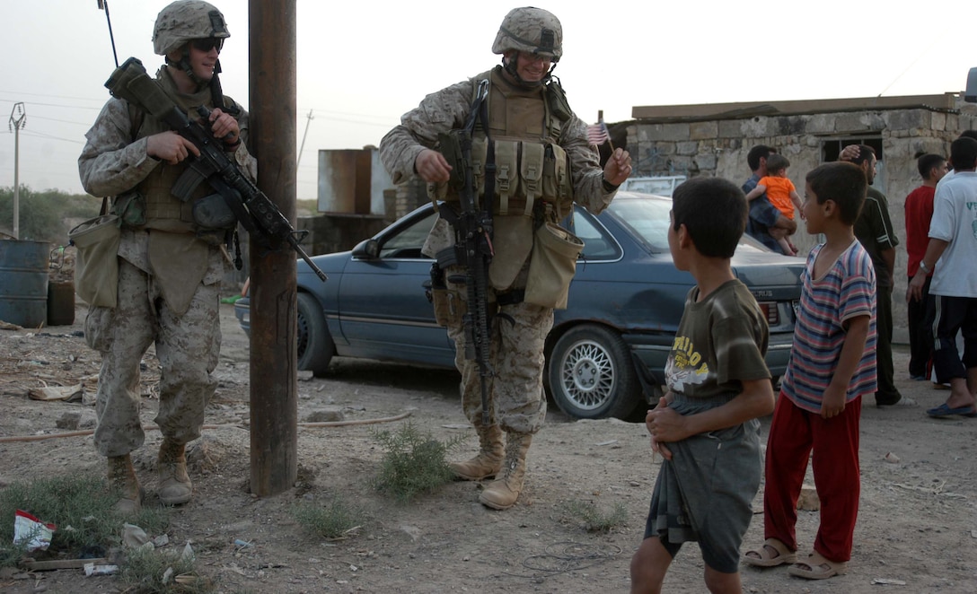 AR RAMADI Iraq (July 19, 2005) - Sergeant Aaron P. Selby, 3rd Squad leader, 1st Platoon, Company C, 1st Battalion, 5th Marine Regiment, entertains two Iraqi children by waving a small American flag during a mission in the city here July 19. His comrade, Lance Cpl. Nicolas W. Eckel, a 20-year-old rifleman with the squad and Las Vegas, Nev., native stands by and smiles. Selby, a 26-year-old from Ft. Thomas, Ky., is a husband a father of two. Nicole, his wife of six years, their three-year-old daughter Amara and two-year-old son Memphis are at home in Oceanside, Calif., while he fights the war on terror halfway around the world. The Selbys will be reunited in October after seven months of separation when 1st Battalion, 5th Marines return to Camp Pendleton, Calif. Photo by: Cpl. Tom Sloan