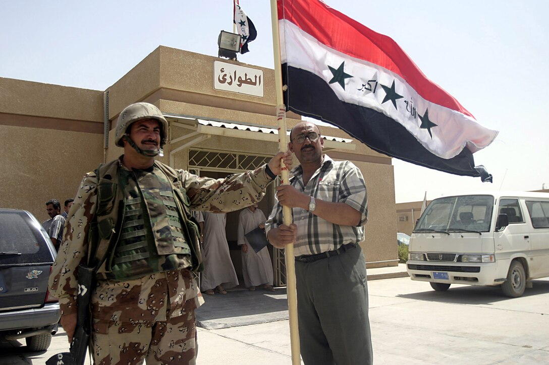 Hit, Al Anbar, Iraq - The commanding officer of Company 1, Col. Mahdi A. Mohammed, a 39-year-old Mosul native, hands the hospital administrator a new flag to replace the hospital's torn one during a visit to distribute surplus medical supplies to clinics in the area. (Official USMC Photo by Corporal Ken Melton)