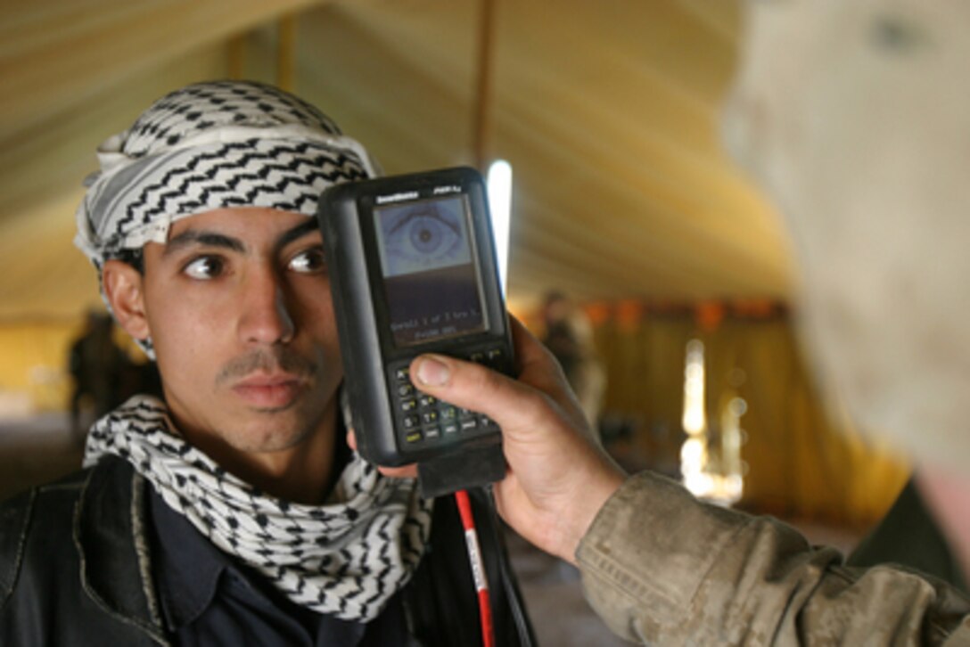 Marine Lance Cpl. Luis Molina scans an Iraqi citizen's retina at Brahma Park in Fallujah, Iraq, on Jan 25, 2005. U.S. Marines are utilizing a Biometric Analysis Tracking System to record and identify Iraqi civilians entering the battle torn city of Fallujah in an attempt to find and identify insurgent forces. The tracking system uses thumbprints, a photograph of the face, and a retinal scan to establish positive identity. Molina is deployed with Marine Wing Support Squadron 373 in support of Operation Iraqi Freedom. 