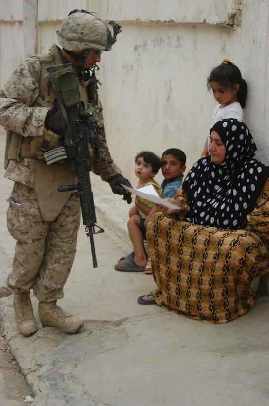 AR RAMADI Iraq (June 29, 2005) -Sergeant Joe A. Salinas, squad leader for 3rd Squad, 4th Platoon, Company B, 1st Battalion, 5th Marine Regiment, hands an Iraqi woman a coalition forces flier during a mission in the city here June 28. The 35-year-old from San Antonio, Texas and his fellow Marines conducted a patrol through a portion of their company's area of operations to locate enemy sniper positions. Company B's observation post has been taking sporadic sniper fire from the area around it. Photo by: Cpl. Tom Sloan