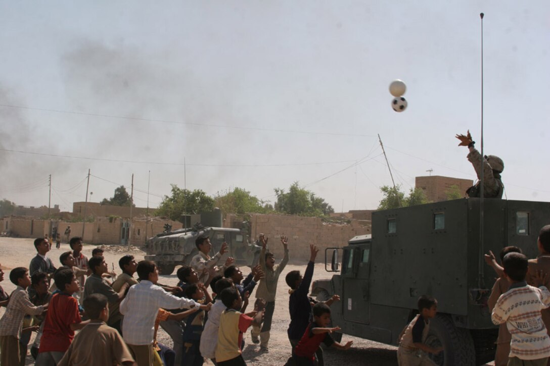 050929-M-2607O-004 AL ANBAR PROVINCE, Iraq -- A Marine from 6th Civil Affairs Group throws soccer balls to local children during a visit to a project site on Sept. 29.  On almost every trip 6th CAG makes into the Area of Operation they give away school, sporting and hygiene supplies to the local population.