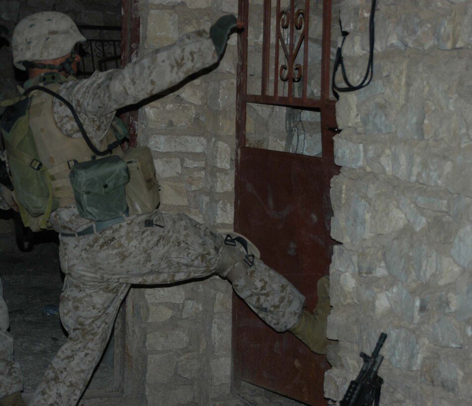 AR RAMADI, Iraq (March 29, 2005) -With a hard, right kick, 20-year-old Lance Cpl. Bradford L. Dunn, squad automatic gunner, 3rd Squad, 2nd Platoon, Company C, 1st Battalion, 5th Marine Regiment, from Covington, Ky., becomes a human battering-ram and breaches the entry to an abandoned building his Marines will use as an over watch. Marines with 2nd Platoon, Company C, 1st Battalion, 5th Marines, conducted a late-night combat patrol in a portion of the city here where groups of Iraqis, possibly insurgents, have been seen gathering after curfew hours, which are from 10 p.m. and 6 a.m. The Marines discovered a group of Iraqi teens playing soccer beneath a streetlight and several adults gathered in the street in front of their residences. The Marines finished the patrol without incident and returned to their base camp at Snake Pit. Photo by Cpl. Tom Sloan