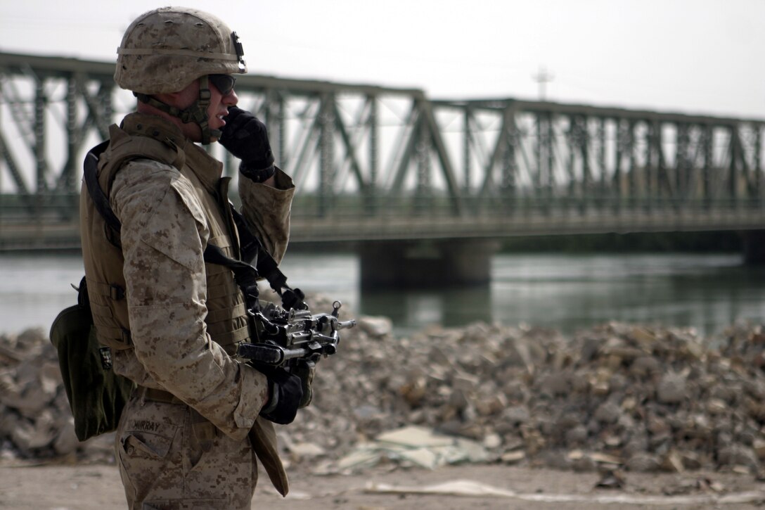 FALLUJAH, Iraq - Pfc. Andrew Murray, a squad automatic weapon gunner with 1st Platoon, Company C, 1st Battalion, 6th Marine Regiment, talks on the radio while providing security alongside the Euphrates River here July 24.  The unit is currently working alongside Iraqi Security Forces to conduct security and stability operations throughout Fallujah.