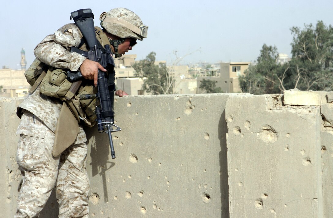 FALLUJAH, Iraq - Cpl. Justin Slep, a team leader with 1st Platoon, Company C, 1st Battalion, 6th Marine Regiment, peers over a ledge on a rooftop here July 24 while patrolling the city streets.  Company C is currently working alongside Iraqi Security Forces to conduct security and stability operations throughout Fallujah.