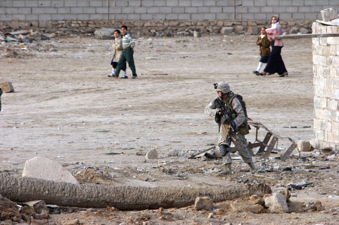 AR RAMADI, Iraq (November 30, 2005) - A Marine from 3rd Battalion, 7th Marine Regiment, runs to cover while parents walking their children to school look on during Taskforce Block Party Six Nov. 30. Photo by Cpl. Shane Suzuki