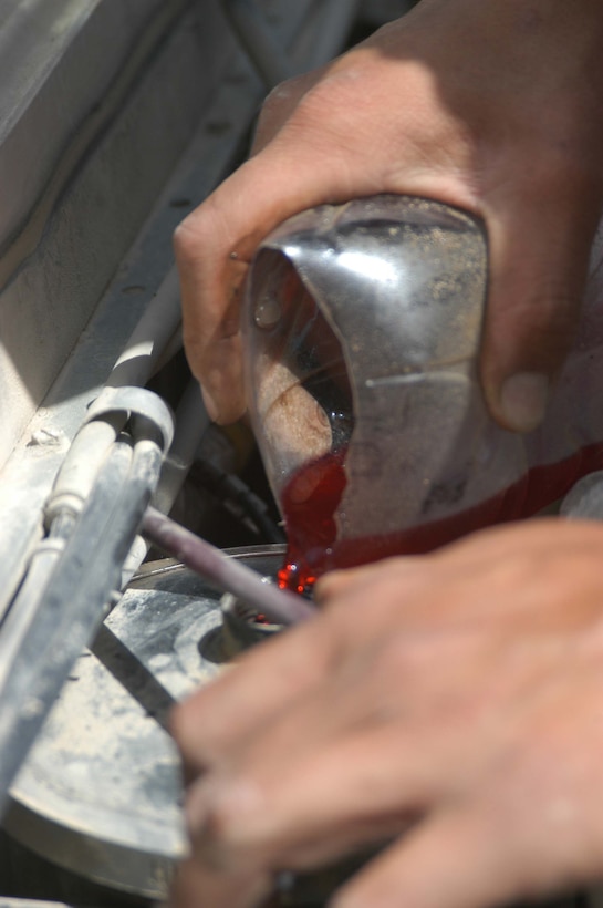 CAMP HURRICANE POINT, Ar Ramamdi, Iraq (March 31, 2005) -Twenty-one-year-old Cpl. Michalson Bahe of Casa Grande, Ariz., a motor transportation mechanic with Headquarters and Service Company, 1st Battalion, 5th Marines, pours power steering fluid into a humvee brought to his garage by a Marine with Weapons Company who said the vehicles steering wheel wouldn't turn while stationary. Bahe and Pfc. David S. Johnson, who's also a motor T mechanic, boast a 24-hour turn around time on all the vehicles they work on. The two grease monkeys are responsible for maintaining and repairing 90 of the infantry battalion's vehicles. They stay on call during the night and routinely find themselves burning the midnight oil fixing humvees and 7-tons at their shop. Photo by Cpl. Tom Sloan