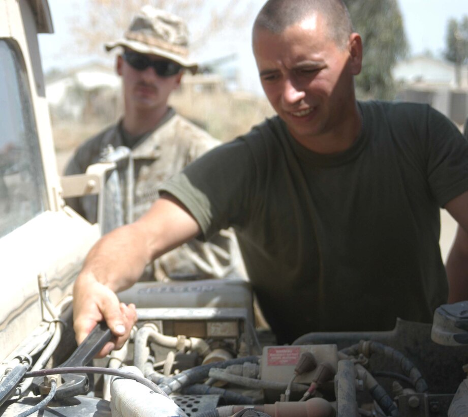 CAMP HURRICANE POINT, Ar Ramamdi, Iraq (March 31, 2005) -Twenty-seven-year-old Pfc. David S. Johnson of Newbaltimore, Mich., a motor transportation mechanic with Headquarters and Service Company, 1st Battalion, 5th Marines, strains as he loosens the bolt on a humvee's power steering container with a wrench. Twenty-one-year-old Lance Cpl. John S. Summers Jr., of Indianapolis, an anti tank assault man and driver for Whiskey 5, Weapons Company, 1st Battalion, 5th Marines, watches from behind. Johnson and Cpl. Michalson Bahe, who's also a motor T mechanic, boast a 24-hour turn around time on all the vehicles they work on. The two grease monkeys are responsible for maintaining and repairing 90 of the infantry battalion's vehicles. They stay on call during the night and routinely find themselves burning the midnight oil fixing humvees and 7-tons at their shop. Photo by Cpl. Tom Sloan