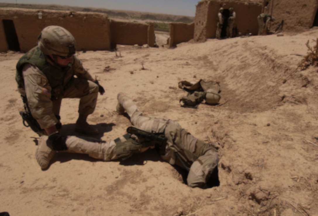 While his buddy keeps a firm grip on his ankle U.S. Air Force Staff Sgt. Phillip Hauser sticks his head in a hole to search for an underground weapons cache near Tuz, Iraq, on June 25, 2005. Hauser is deployed with the 506th Air Expeditionary Group's Explosive Ordnance Disposal team. 