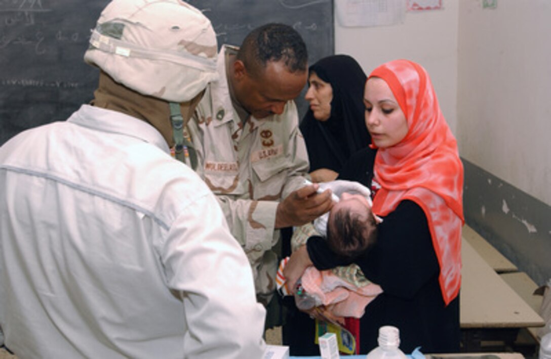 Army Sgt. 1st Class Berhane Woldelassie examines an infant in its mother's arms at a medical clinic set up in the Abu Ghraib neighborhood of Baghdad, Iraq, on July 2, 2005. Woldelassie is deployed with the 11th Armored Cavalry Regiment. 