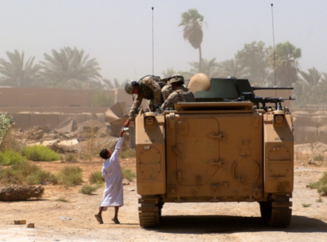 A U.S. Army soldier leans out of his M-113 Armored Personnel Carrier to share his Meal Ready to Eat with an Iraqi boy in Mushada, Iraq, on June 23, 2005. 