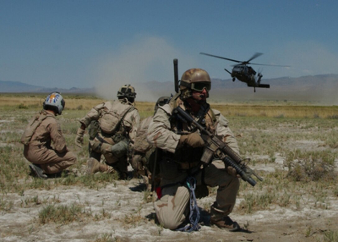 U.S. Air Force Pararescuemen and a simulated survivor watch as an HH-60G Pave Hawk helicopter comes in for landing during a training exercise as part of Desert Rescue in Fallon, Nev., on July 13, 2005. Desert Rescue is a multi-service, multi- national training exercise to prepare combat search and rescue teams to extract downed personnel in a variety of environments and situations. 