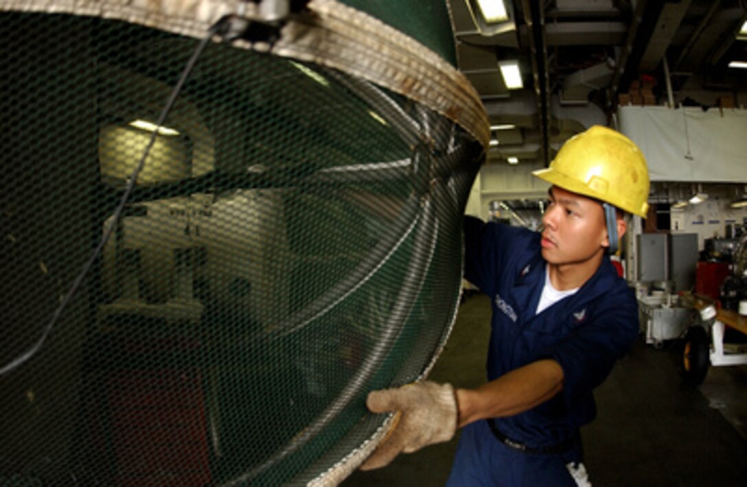 Navy Petty Officer 3rd Class Jalvin Yuchongtian inspects the cover for an J-52 jet engine in the hangar bay of the aircraft carrier USS Nimitz (CVN 68) on July 14, 2005. The cover is placed over the intake of the jet engine to prevent foreign objects from being sucked into the engines during maintenance. Yuchongtian is a Navy aviation machinist's mate onboard the Nimitz. 