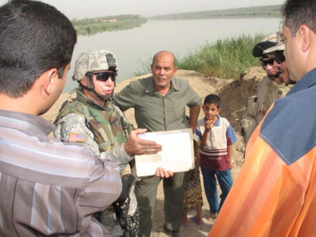 U.S. Army Staff Sgt. Chris Edwards (left) talks to Iraqi contractors along the Tigris River north of Baghdad, Iraq, on July 8, 2005. The contractors are installing a water treatment plant that will provide 3 million gallons of potable water daily to residents in Husseiniya, Iraq. The U.S. Army Corps of Engineers overseeing the project, which includes the construction of a new raw water intake in the river, two submersible pumps and transmission pipe work. Edwards is attached to the 490th Civil Affairs Battalion. 