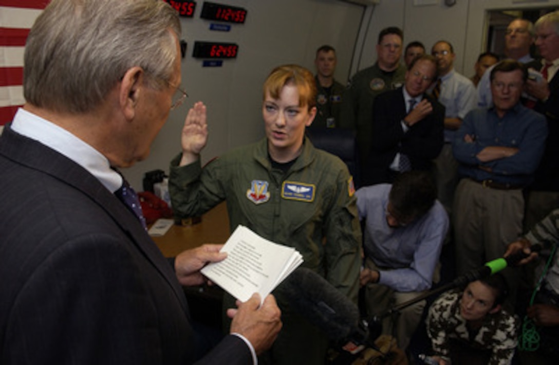 Secretary of Defense Donald H. Rumsfeld (left) performs a reenlistment ceremony for Air Force Senior Airman Brandi Tremmel (center) as members of the media and staff look on at Balad Air Base, Iraq, on July 27, 2005. Tremmel is a flight engineer assigned to the 11th Airborne Command and Communications Squadron, Offutt Air Force Base, Neb. Rumsfeld used the aircraft to make a surprise visit to the troops and senior leadership in Iraq. 