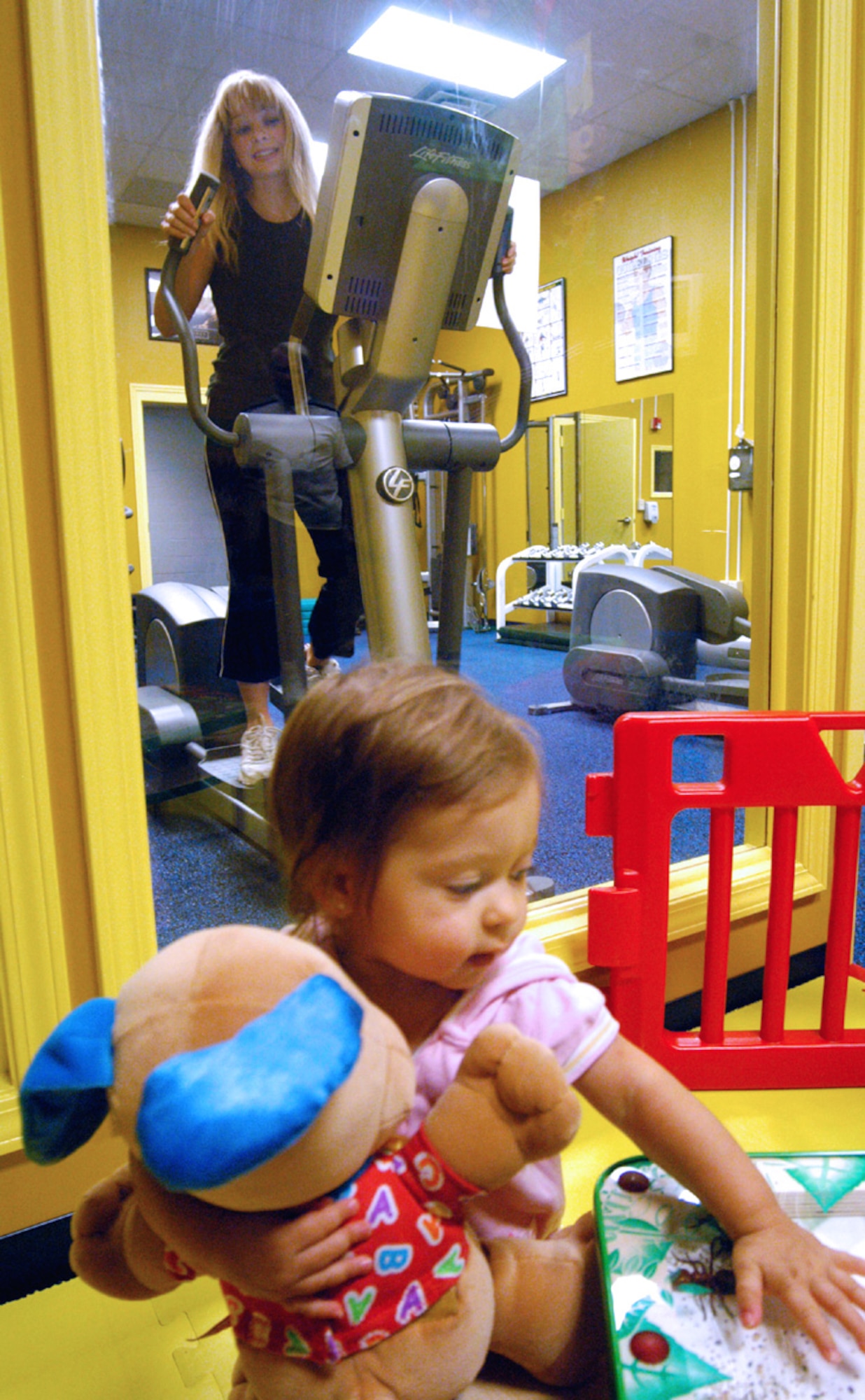 ROBINS AIR FORCE BASE, Ga. -- Bella Zuniga, 1, plays while her mother, Samantha, works out in the new family fitness room here.  (U.S. Air Force photo by Sue Sapp)