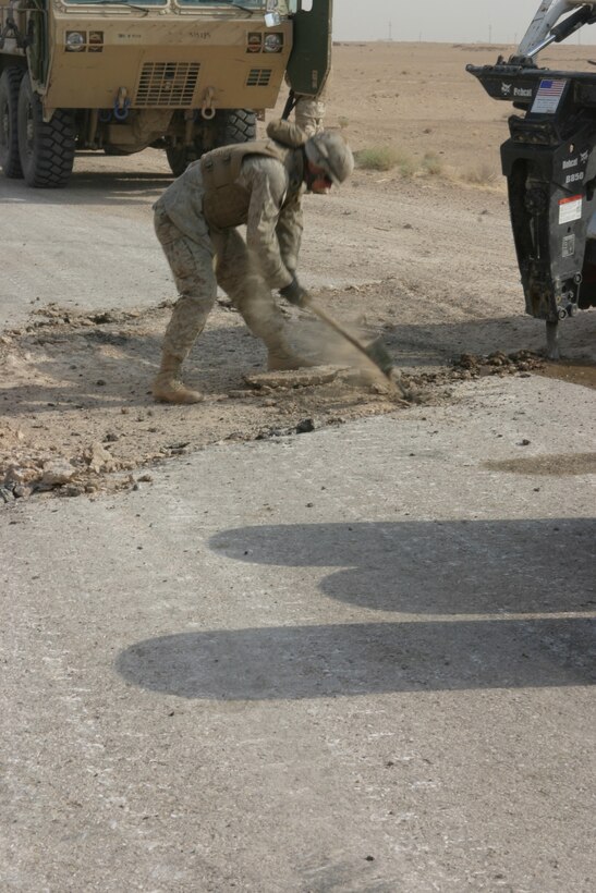 CAMP TAQADDUM, Iraq (June 4, 2005)- Corporal John Clark, a Fowler, Ind., native and heavy equipment operator with Support Company, 8th Engineer Support Battalion, 2d Force Service Support Group (Forward), uses a pick ax to break away existing concrete and debris from a hole on Alternate Supply Route San Juan June 4. The Marines of 8th ESB conducted Operation San Juan, a five-day operation repairing holes Improvised Explosive Devices and heavy travel have caused, making it safer for convoys and local civilians who travel the road on a daily basis.