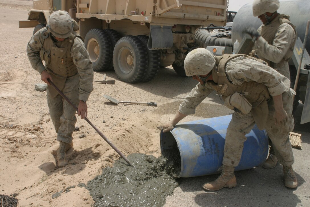 CAMP TAQADDUM, Iraq (June 4, 2005)- Corporal John Clark (left), a Fowler, Ind., native and heavy equipment operator with Support Company, 8th Engineer Support Battalion, 2d Force Service Support Group (Forward), levels out the concrete as Marines dump it to patch a hole June 4 caused by an Improvised Explosive Device. The Marines of 8th ESB conducted Operation San Juan, a five-day operation repairing Alternate Supply Route San Juan, making it safer for convoys and local civilians traveling the road on a daily basis.