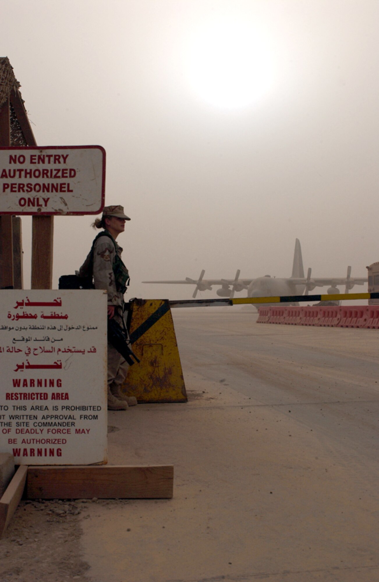 BAGHDAD, Iraq -- Senior Airman Dawn Lister guards the flightline entry control point as a fine, brown dust coats everything following a nightlong sandstorm recently.  A C-130 Hercules sits grounded as a result of poor visibility.  Airman Lister is assigned to the 447th Expeditionary Security Forces Squadron and is deployed from Minot Air Force Base, N.D.  The C-130 is assigned to the 910th Airlift Wing in Youngstown, Ohio.  (U.S. Air Force photo by Tech. Sgt. Brian Davidson)