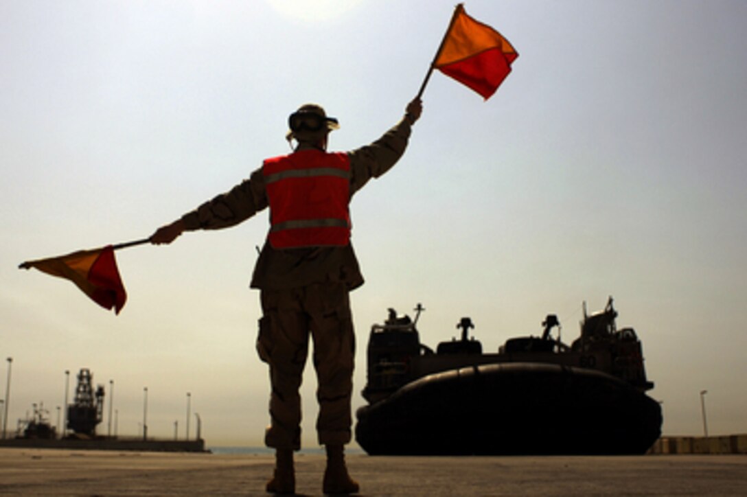 Navy Seaman Charles Shafer, from Beach Master Unit 2, uses flags to signal to the craftmaster of a Navy Landing Craft Air Cushion, or LCAC, at a Kuwaiti Naval Base staging area on June 1, 2005. The LCAC, assigned to Assault Craft Unit 4 based in Little Creek, Va., is deployed in the Northern Persian Gulf with the USS Kearsarge (LHD 3) and USS Ashland (LSD 48) in support of transport operations with the 26th Marine Expeditionary Unit. 