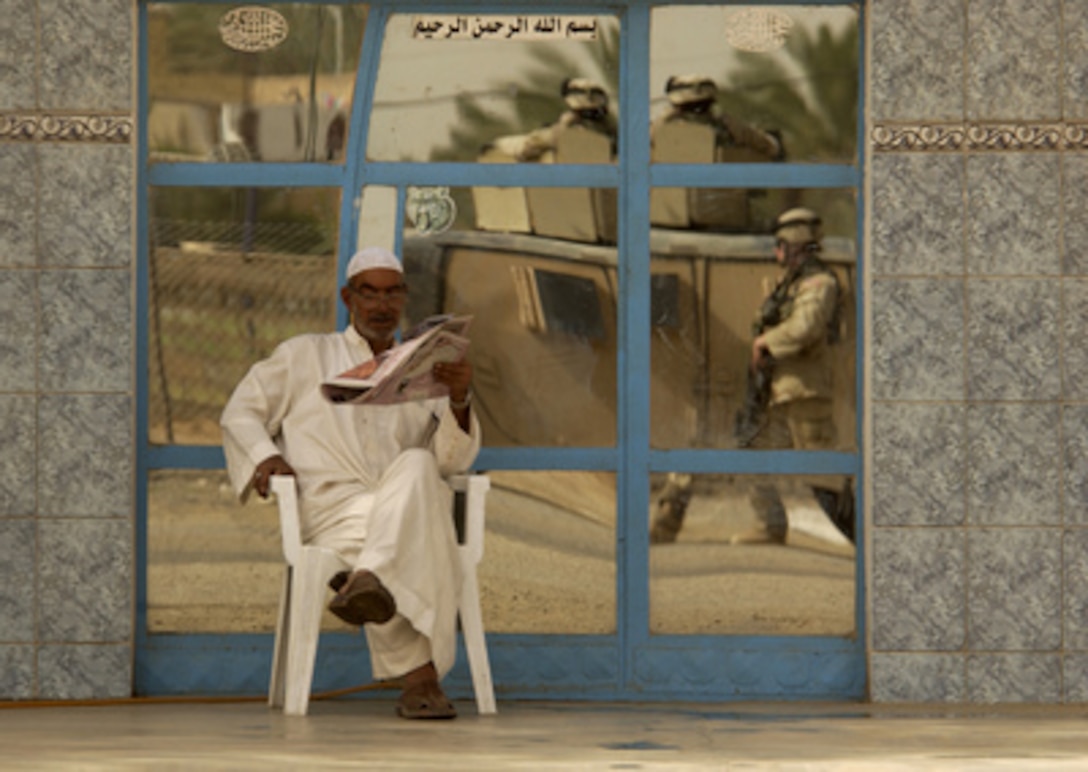 An Iraqi citizen reads a paper while U.S. soldiers patrol the streets in Wajihiyah, Iraq, on June 2, 2005. 