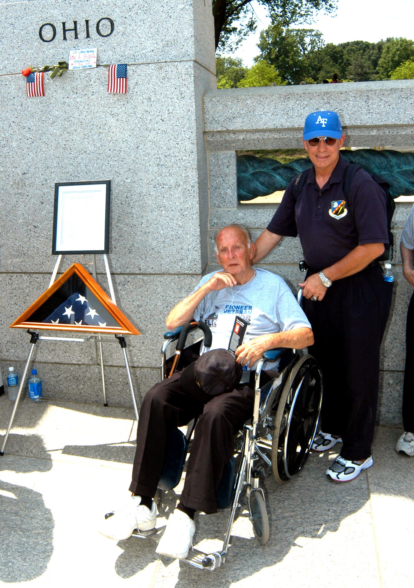 WASHINGTON -- Retired Col. Bob Manning (right) volunteered to help take care of World War II veterans when they visited the National World War II Memorial in Washington on June 11.  The Air Force Academy graduate pushed Elwood Lannon, 84, around the memorial in a wheelchair during the visit.  The American flag on the stand to the left was flown over the national cemetery in Dayton, Ohio, and represents the 400,000 servicemen and women who died during World War II and will never view their memorial.  (Department of Defense photo by Rudi Williams)