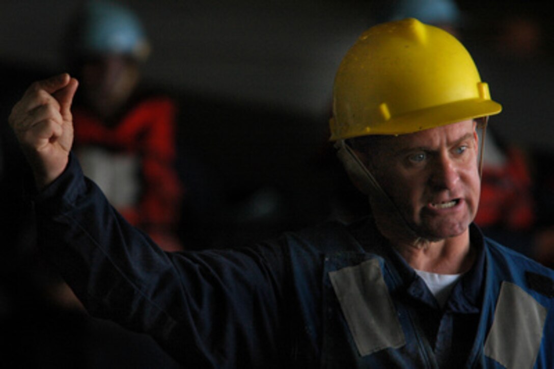 Petty Officer 2nd Class Donald McGinly signals to raise a pallet of supplies as the aircraft carrier USS Kitty Hawk (CV 63) offloads equipment to the underway replenishment oiler USNS Tippecanoe (T-AO 199) during a replenishment at sea on June 11, 2005. The underway replenishment allows fuel for ships and aircraft and stores to be transferred from ship-to-ship, extending their at sea capabilities. 