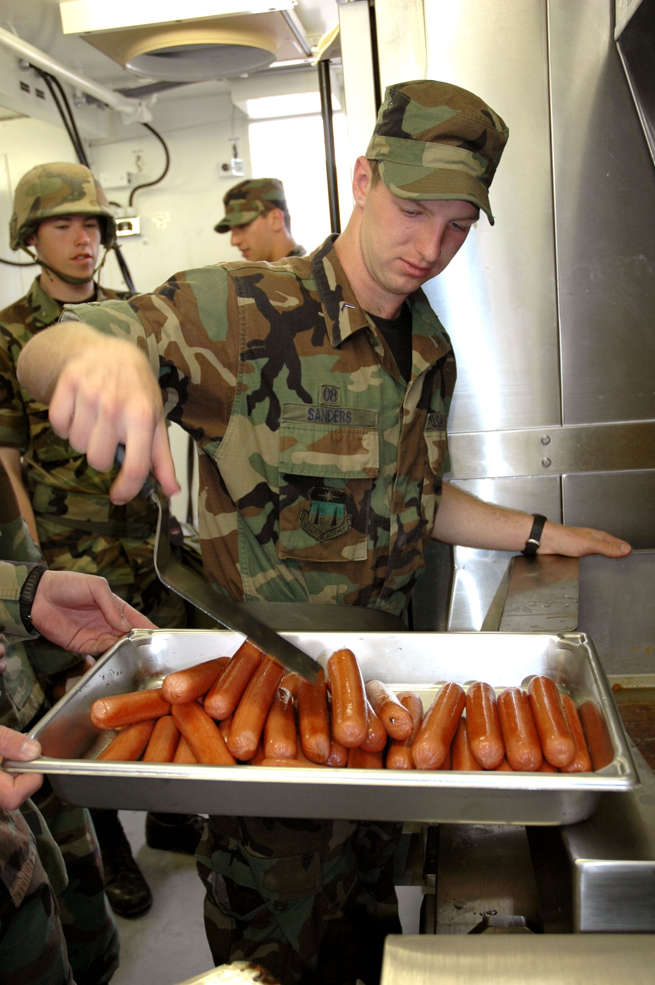 U.S. AIR FORCE ACADEMY, Colo. -- Cadet 3rd Class Kyle Sanders prepares hot dogs in a contingency deployment kitchen June 10 as the cadets' first hot meal during Global Engagement 2005.  The kitchen can be set up in two hours.   This was the first of six groups of cadets to go through the training throughout the summer.  (U.S. Air Force photo by Tech. Sgt. Matt Gilreath)