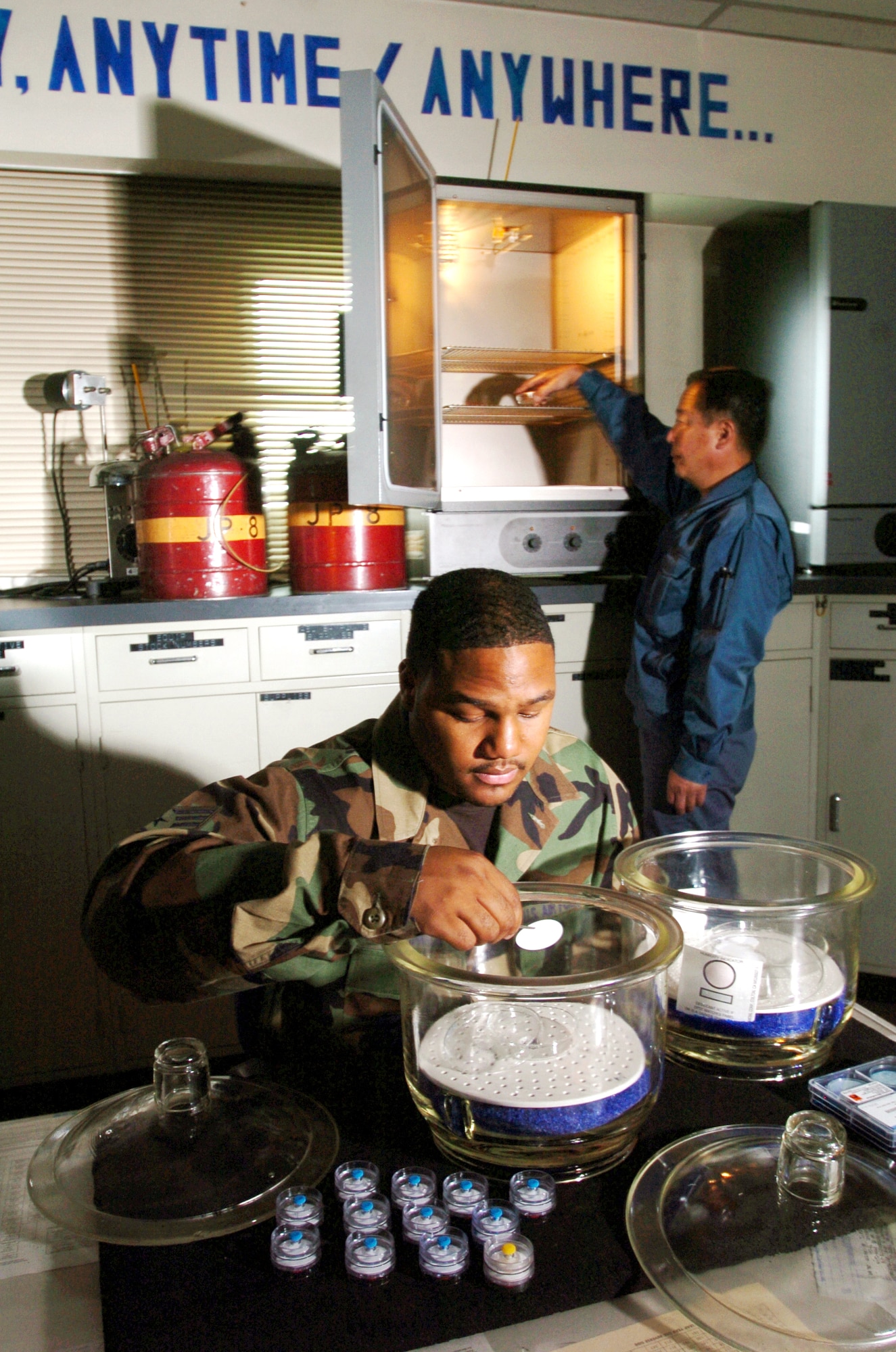 YOKOTA AIR BASE, Japan -- Staff Sgt. Carmarius Johnson conducts a fibers test of a jet fuel sample from a fuel truck while Susumo Iwasaki places fuel filters in an oven during inspection here.  They are inspecting the filters to ensure they are free of contaminants.  They are fuels laboratory technicians with the 374th Logistics Readiness Squadron here.  (U.S. Air Force photo by Master Sgt. Val Gempis)